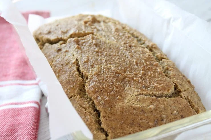 Close up of baked keto bread in clear loaf pan lined with white parchment paper with red dish cloth beside it