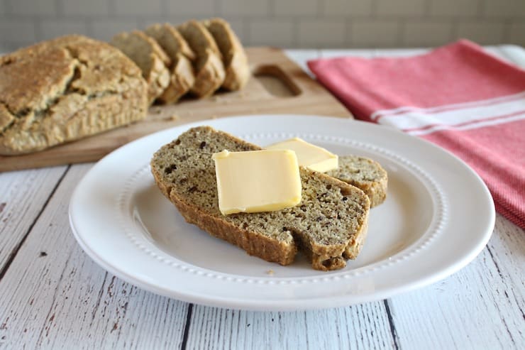 Slices of keto bread with slabs of butter on them on white plate with loaf in background