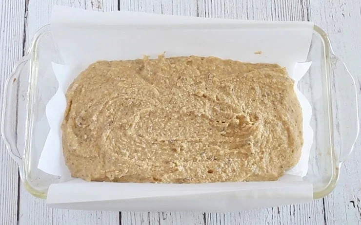 uncooked keto bread recipe dough in clear loaf pan lined with white parchment paper
