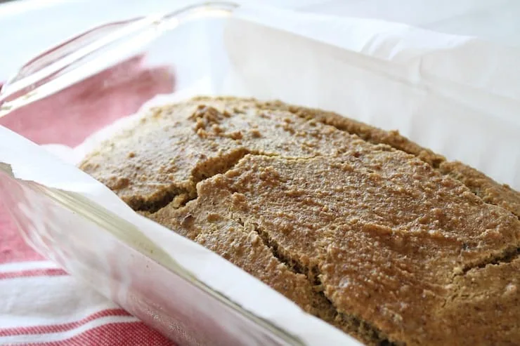 Close up of baked keto bread in clear loaf pan lined with white parchment paper with red dish cloth beside it