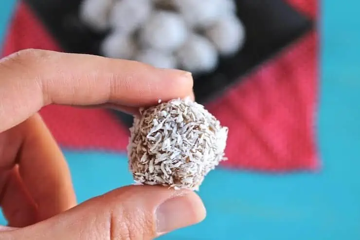 Close up of hand holding a coconut date ball in between two fingers