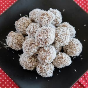 A pile of coconut date balls on a black plate on top of a red mat with white polka dots