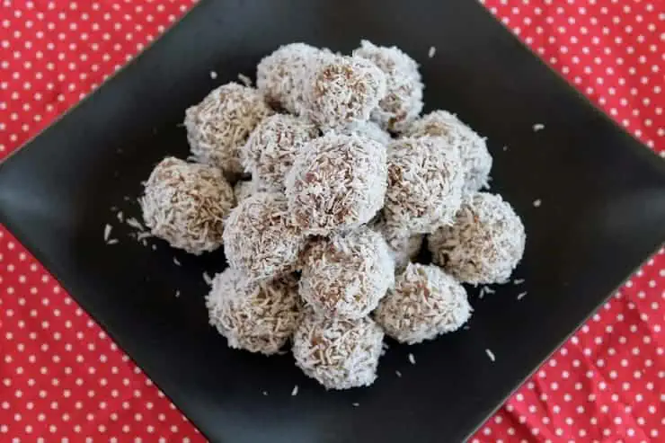 A pile of coconut date balls on a black plate on top of a red mat with white polka dots