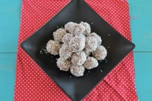 A pile of coconut date balls on a black plate on top of a red mat with white polka dots on a blue table