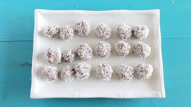 Finished rolled coconut date balls on a white rectangle plate on a blue table