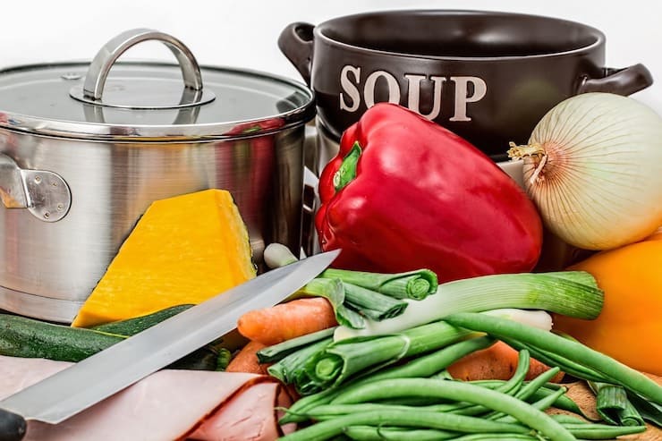 Collection of colorful vegetables with a knife beside it in front of a soup pot