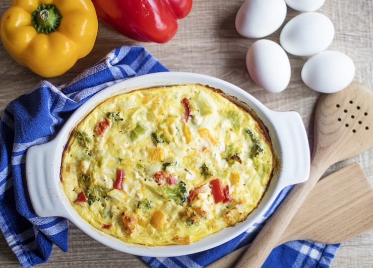 Vegetable frittata in a white casserole dish with ingredients surrounding it
