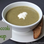 A close up of a bowl of broccoli soup in a white bowl with a slice of bread at the side