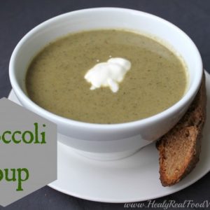 A close up of a bowl of broccoli soup in a white bowl with a slice of bread at the side