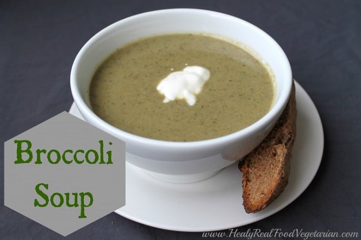 A close up of a bowl of broccoli soup in a white bowl with a slice of bread at the side