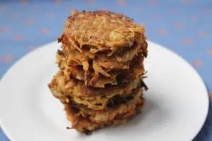 Closeup of several sweet potato latkes stacked on top of eachother on a white plate with a blue background