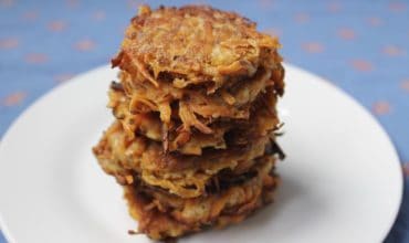 Closeup of several sweet potato latkes stacked on top of eachother on a white plate with a blue background
