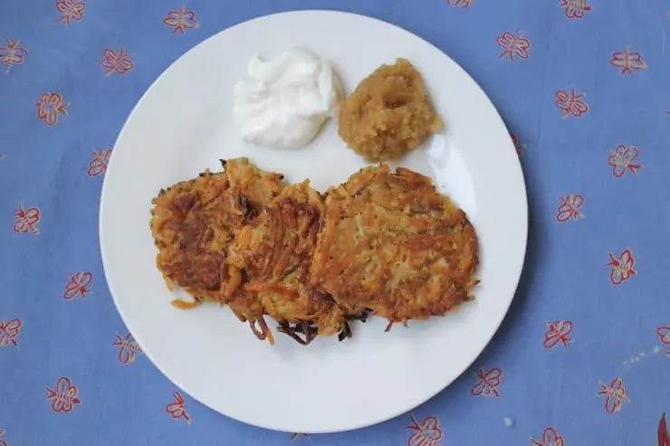 overhead view of white plate with 3 latkes on it with a dollop of sour cream and applesauce over a blue tablecloth