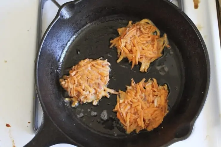 overhead view of black cast iron skillet on the stove with 3 latkes cooking in it