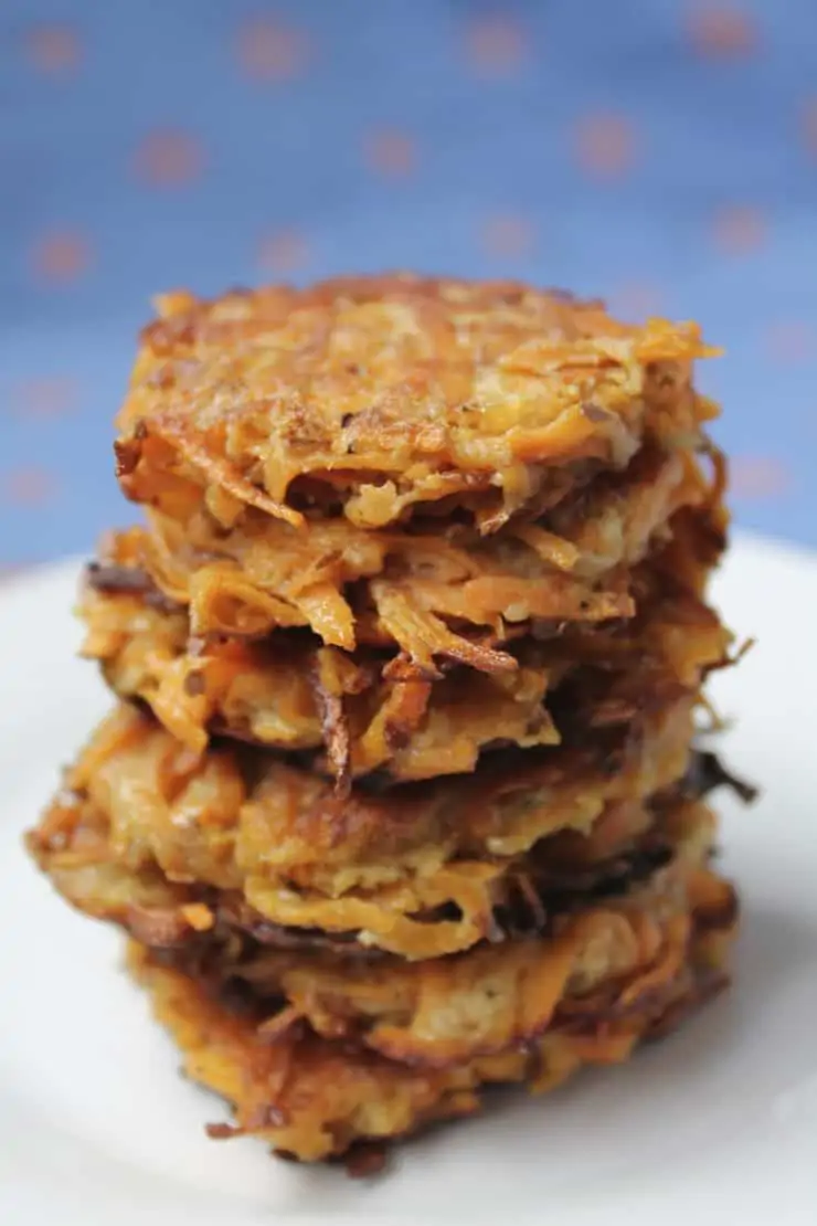 Closeup of several sweet potato latkes stacked on top of eachother on a white plate with a blue background