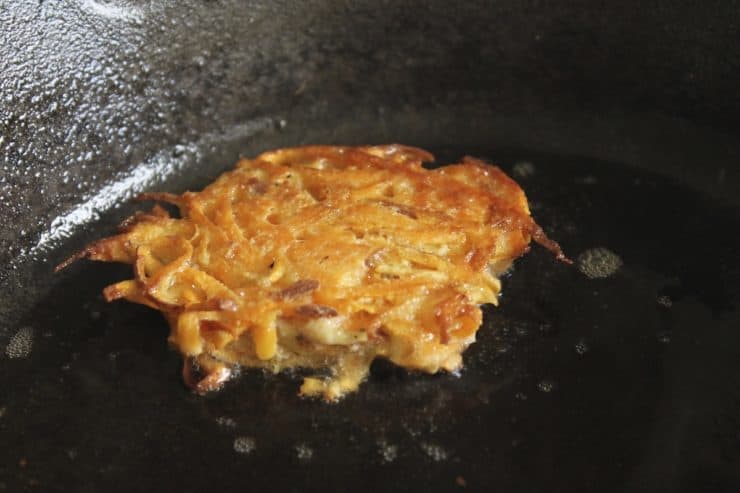 Close up of latke cooking in a black cast iron skillet