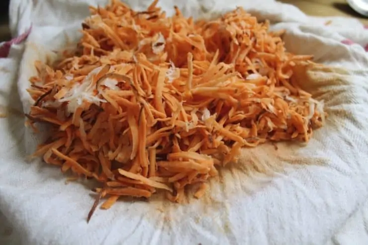 Uncooked shredded sweet potato and onion on a white dishcloth