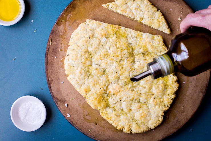 Overhead view of paleo flatbread on a baking stone with olive drizzling over it