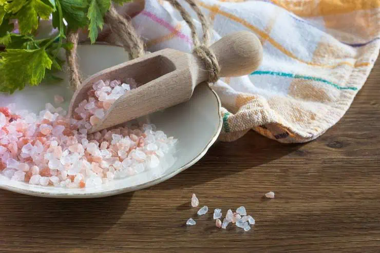 Pink himalayan rock salt on a plate with a wooden scoop on a wooden table