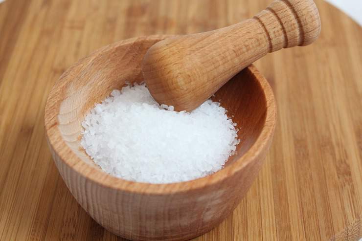 Wooden bowl of white rock salt on a wooden table