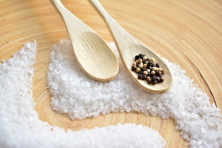 White rock salt on a wooden surface with wooden spoons on top of it