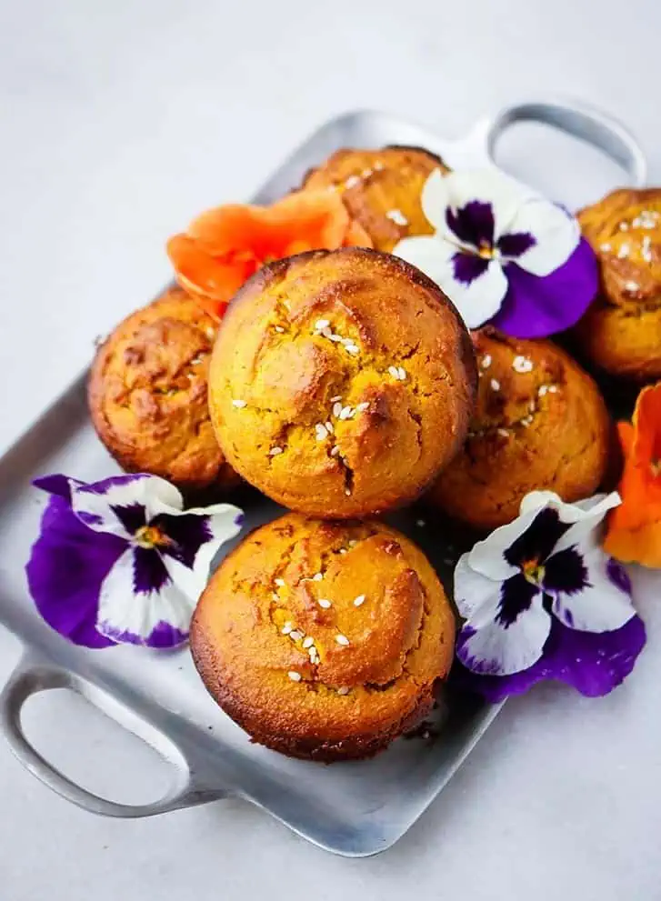 Stacked turmeric cakes on a white plate with white and purple flowers around them