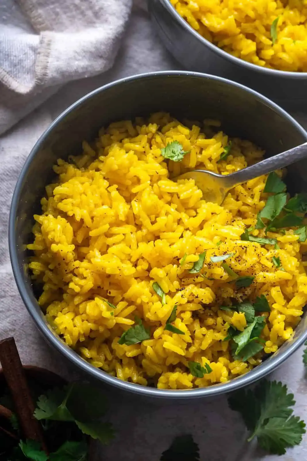 Bowl filled with yellow colored rice with green herbs inside and a spoon inside