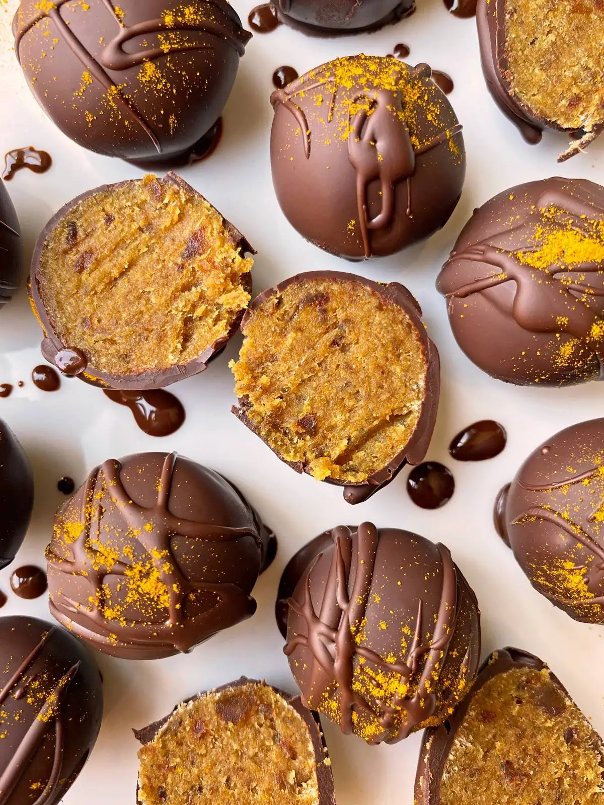 turmeric caramel balls coated in chocolate on a white surface with drizzled chocolate around it