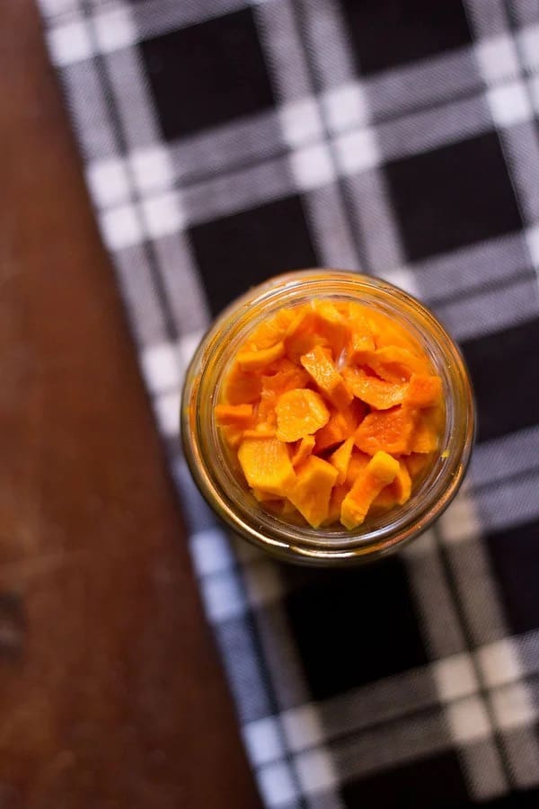 overhead shot of pickled turmeric in a clear jar on top of a plaid cloth on a table