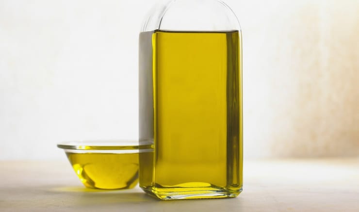 Clear glass bottle of olive oil with clear small bowl of olive oil next to it