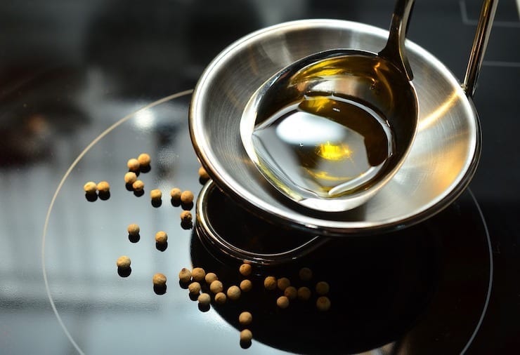 Stainless steel bowl with oil being ladled into it on a black counter