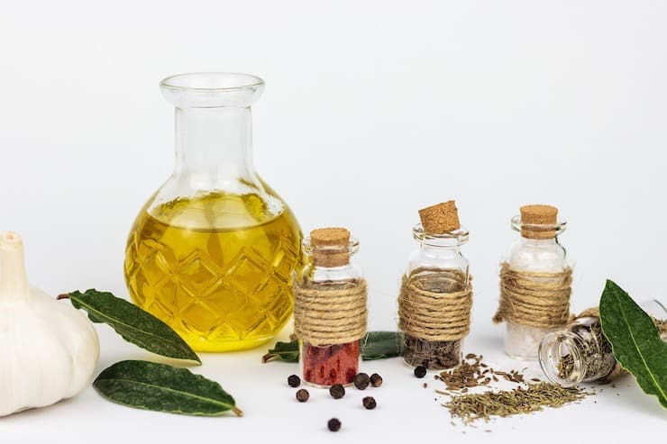 Clear glass bottle of oil surrounded by herbs and spices
