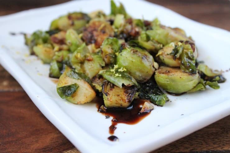 Close up of cooked brussels sprouts with balsamic glaze on a white plate