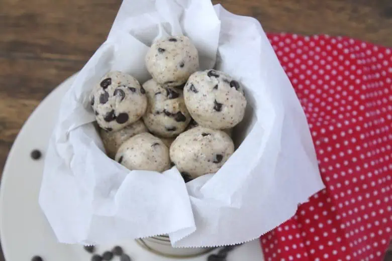 Keto cookie dough fat bombs in a gold container lined with white paper with a red napkin with white polka dots next to it