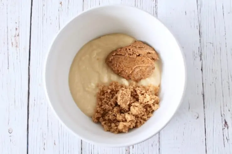 Separate dollops of coconut butter, nut butter and sweetener in a white bowl on a white wooden surface