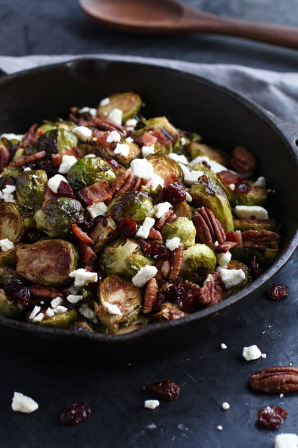 A close up of Brussels sprouts in a black bowl with feta, bacon and pecans