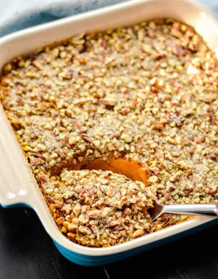 A close up of a sweet potato casserole with a spoonful getting scooped out