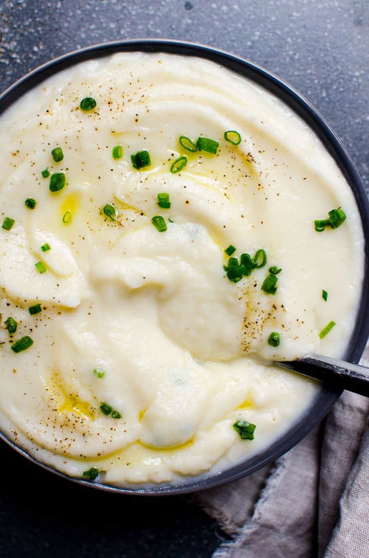 A close up of cauliflower mash in a bowl topped with a drizzle of oil and herbs