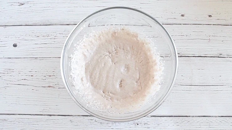 Clear glass bowl on a white wooden surface with white mixed icing inside