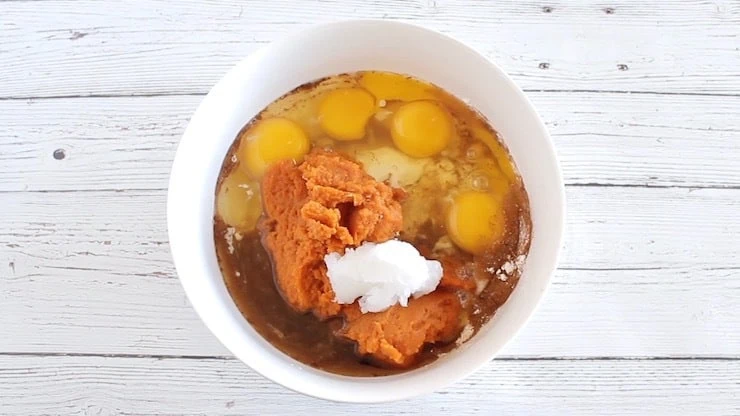 White bowl filled with unmixed paleo pumpkin bread ingredients on a white wooden surface