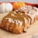Sliced loaf of healthy paleo pumpkin bread with white icing on top on wooden cutting board with small pumpkins in the background