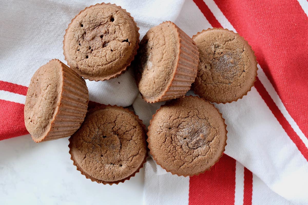 Overhead shot of six chocolate muffins gathered together on a white and red striped dish towel