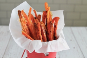 Carrot fries in a small red bucket lined with parchment paper on a white table