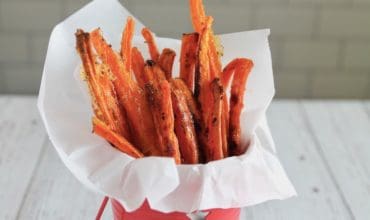 Carrot fries in a small red bucket lined with parchment paper on a white table