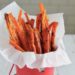 Carrot fries in a small red bucket lined with parchment paper on a white table