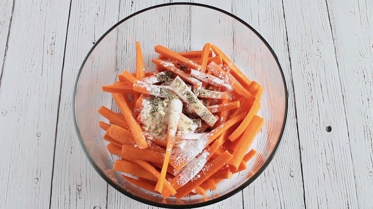 sliced carrots in a clear bowl with spices and flour on top of them