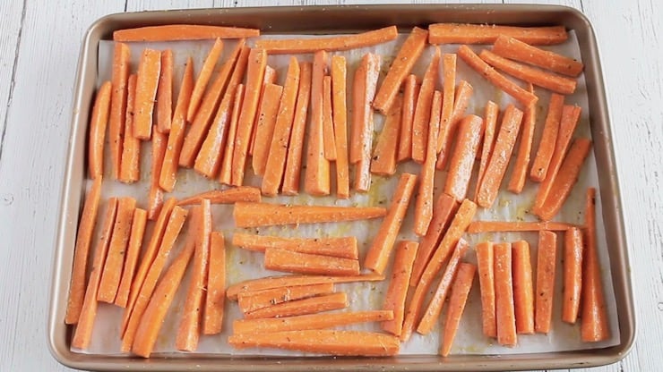 Uncooked sliced carrots on a baking sheet lined with parchment paper