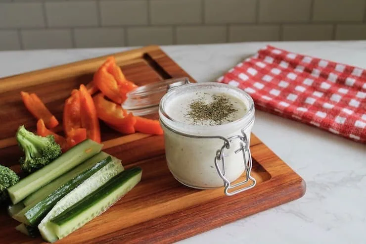 paleo ranch dressing in a jar on a wooden cutting board with sliced vegetables next to it