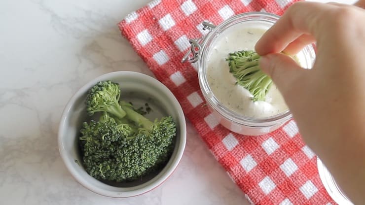 Hand dipping broccoli piece in paleo ranch dressing