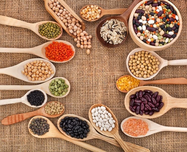 An overhead shot of wooden spoons filled with different grains and beans